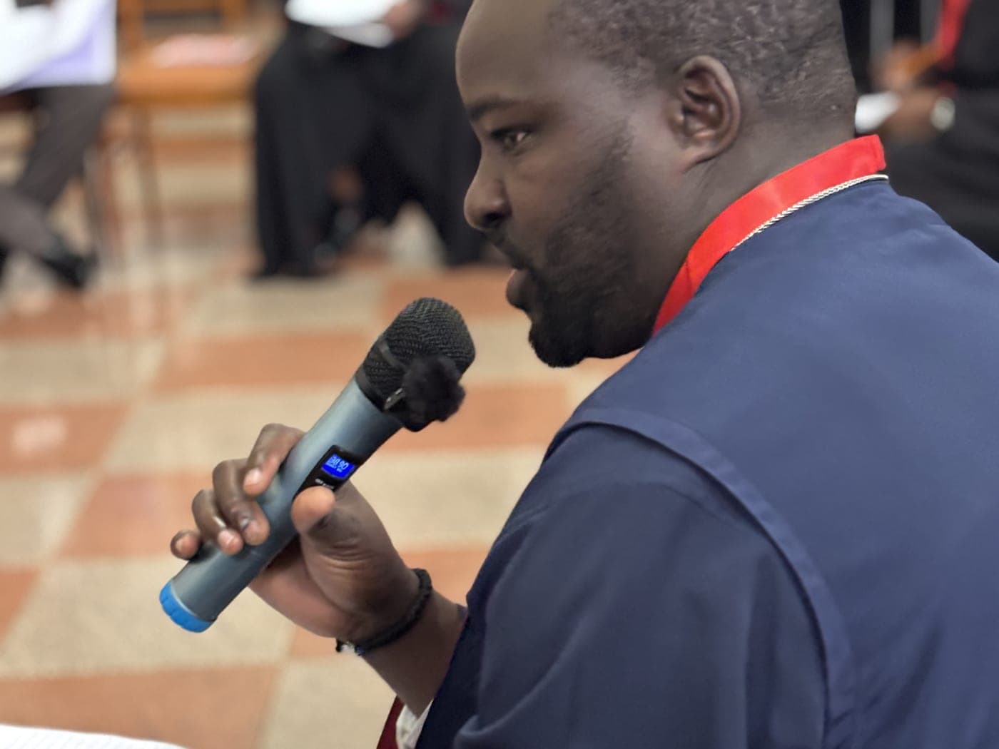 A participant speaking into a hand-held microphone, his notes held open in his other hand.