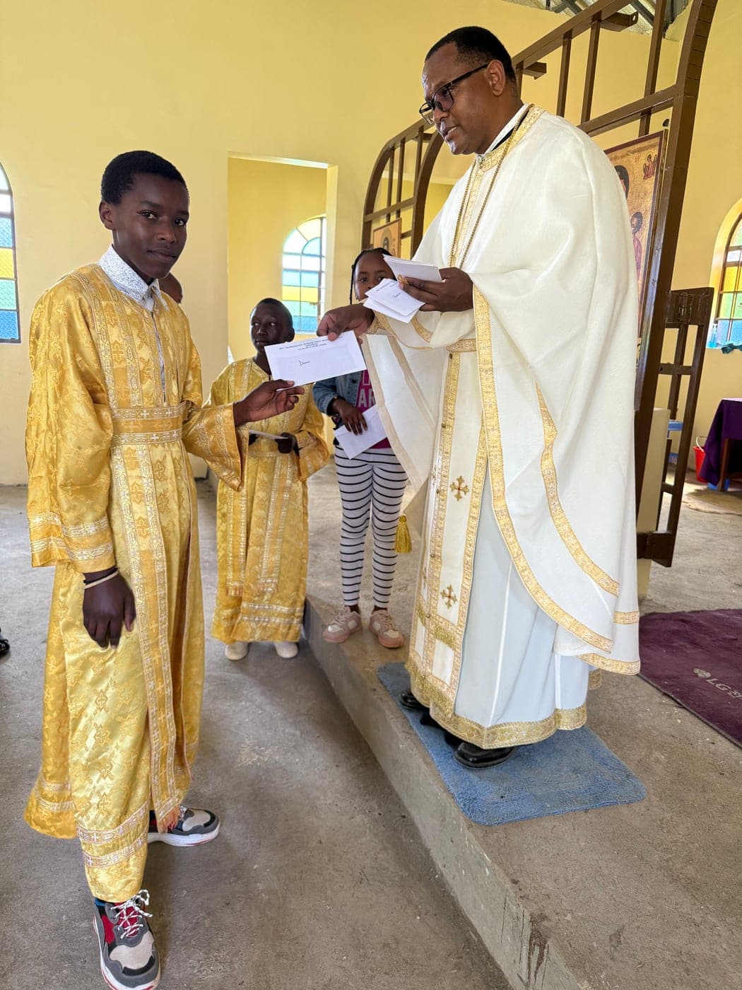 An altar server in gold vestments receiving his award letter from Fr Thiani.