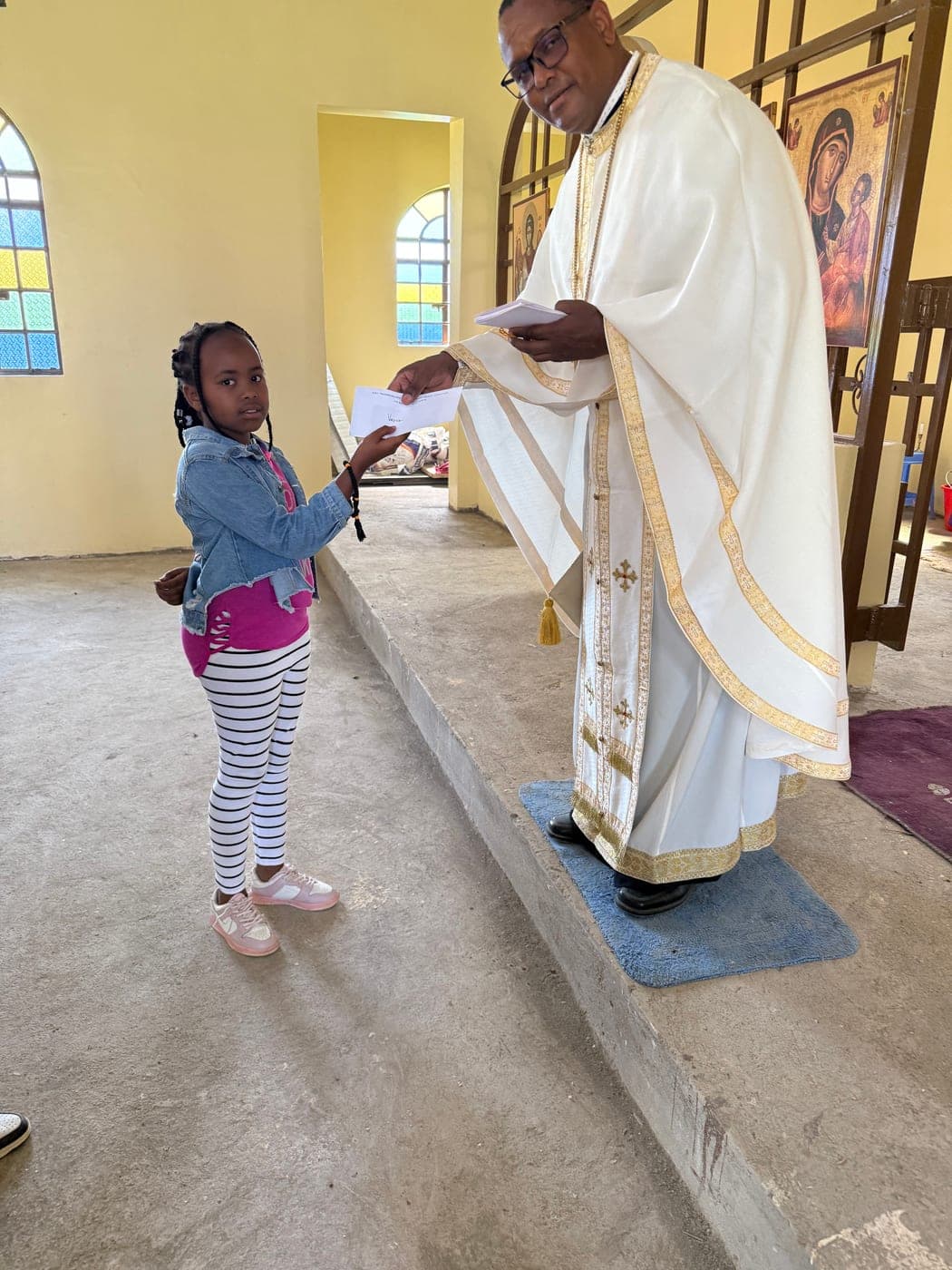 A young girl taking her award letter from Fr Thiani at the foot of the sanctuary steps.