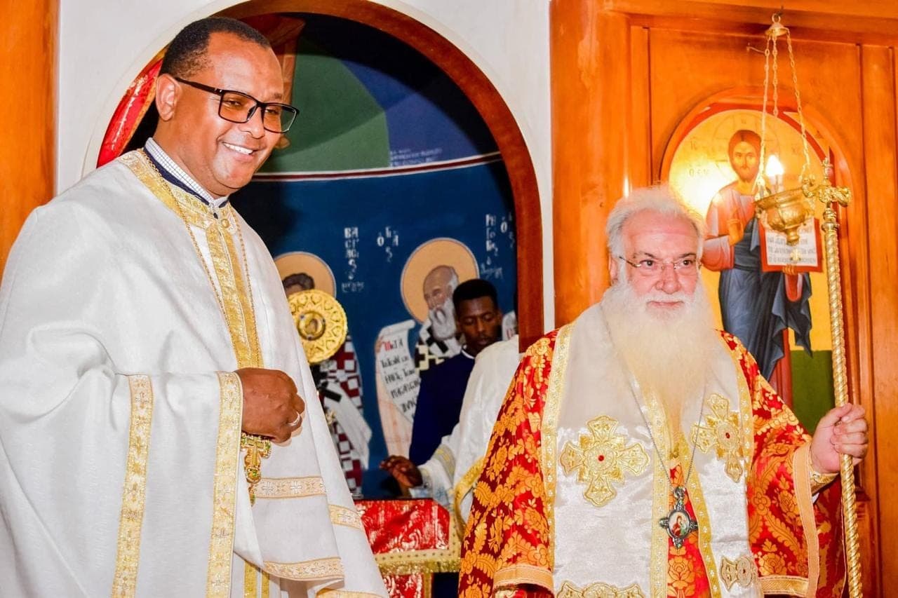 Fr Thiani serving in white and gold vestments alongside Archbishop Makarios.