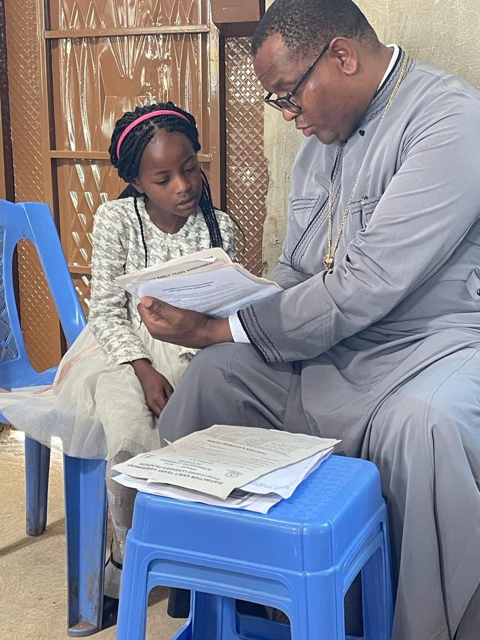 A pupil watching as Fr Thiani reads her early-years assessment sheet.