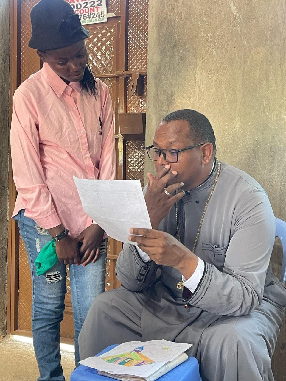 A student standing at Fr Thiani's shoulder while he reads her report closely.
