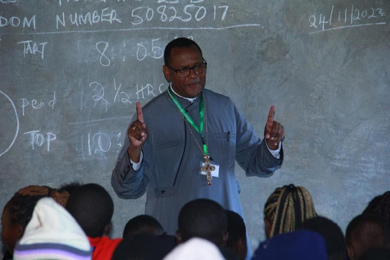 Fr Dr Evangelos Thiani teaching a full classroom of students at a blackboard.