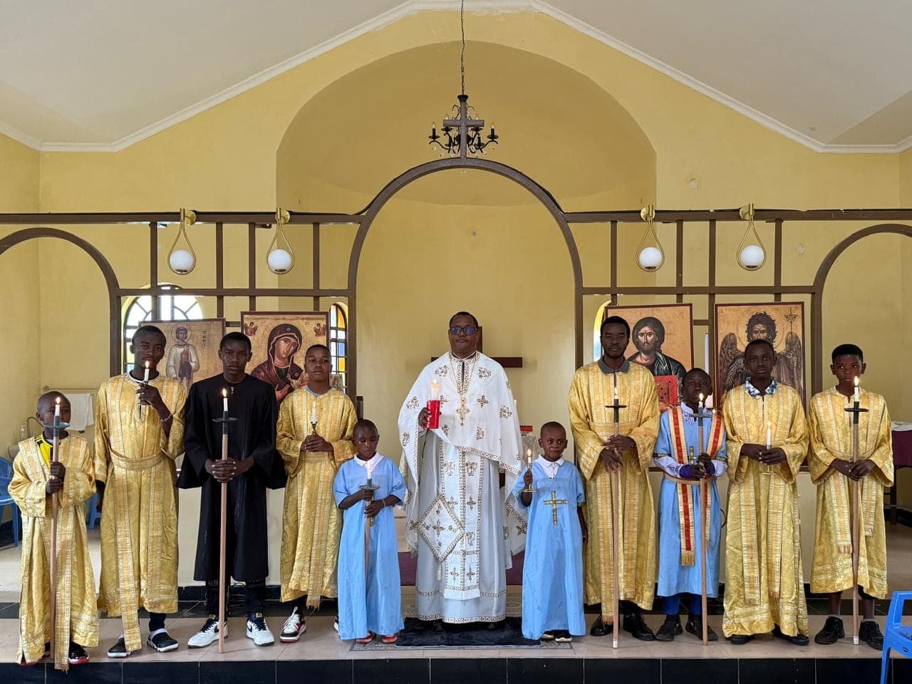 Fr Thiani in white vestments with altar servers holding candles and processional crosses.